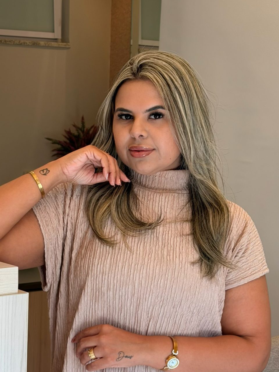 Dra. Najara Vieira, fisioterapeuta especialista em estética avançada, sorrindo levemente para a câmera, com blusa rosé, na recepção do seu consultório