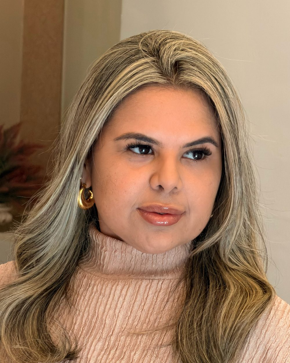Retrato da Dra. Najara Vieira em close, com cabelos longos loiros, brincos dourados e expressão serena, olhando para o lado